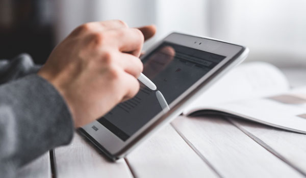 Person sitting at a table using a stylus on a tablet screen.