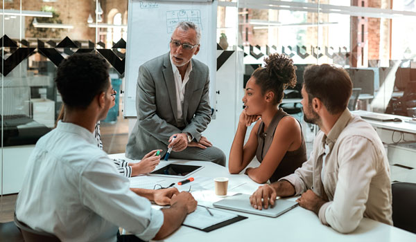 A group of coworkers sit around a conference table with notebooks and tablets.